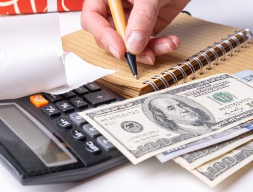 a woman's hand writing down the cash flow in a notebook with a pen, counting cash on a calculator
