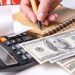 a woman's hand writing down the cash flow in a notebook with a pen, counting cash on a calculator